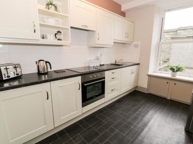 A kitchen with white cabinets a black countertop a toaster kettle oven sink and a window with a plant at Rose Suite in Barmouth