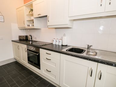 A kitchen with white cabinets a black countertop a sink an oven a toaster and a kettle at Rose Suite in Barmouth
