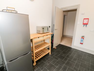 A kitchen with a refrigerator wooden shelving unit with a microwave and an open door at Rose Suite in Barmouth