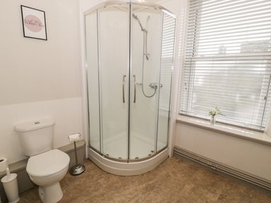 A bathroom with a shower enclosure a toilet a window with blinds and a small vase with flowers on the windowsill at Rose Suite in Barmouth