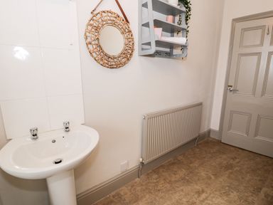 A bathroom with a sink a round mirror a wall-mounted shelf and a radiator at Rose Suite in Barmouth