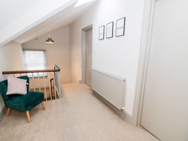 A hallway with a chair and pillow near a window and staircase with three framed pictures above a radiator at Rose Suite in Barmouth