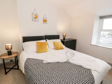 A bedroom with a double bed with yellow pillows and two lamps on side tables at Rose Suite in Barmouth