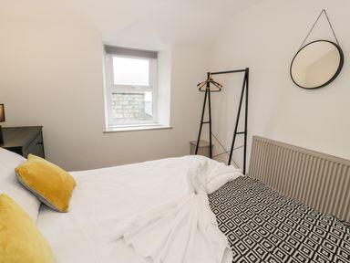 A bedroom with a window a bed with yellow pillows and a black and white blanket a round mirror and a black clothes rack at Rose Suite in Barmouth