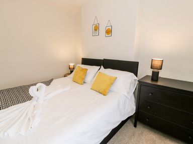A bedroom with a double bed two yellow pillows two bedside lamps and a black dresser at Rose Suite in Barmouth