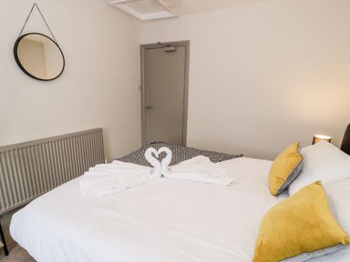 A bedroom with a bed featuring yellow pillows and towel swans next to a gray door and round mirror at Rose Suite in Barmouth