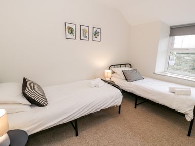 A bedroom with two single beds, pillows, bedside tables with lamps, three framed leaf prints on the wall, and a window at Rose Suite in Barmouth