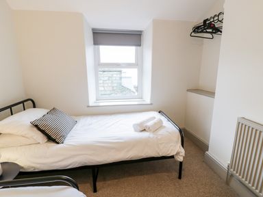 A small bedroom with a single bed with white bedding and striped pillow next to a window with a gray roller blind and wall-mounted hangers at Rose Suite in Barmouth
