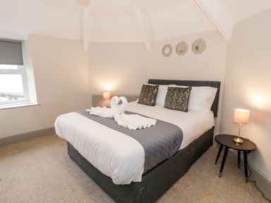 A bedroom with a double bed with pillows and towel swans and two bedside tables with lamps at Rose Suite in Barmouth