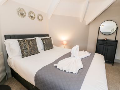 A bedroom with a bed with decorative pillows and folded towels with a black cabinet with a round mirror at Rose Suite in Barmouth