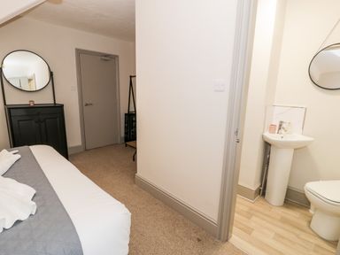 A bedroom with a bed a black cabinet round mirror and ensuite bathroom at Rose Suite in Barmouth