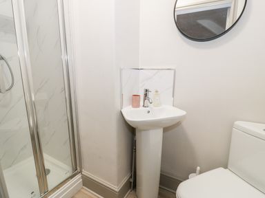 A bathroom with a shower enclosure a pedestal sink with soap and a cup a round mirror and a toilet at Rose Suite in Barmouth