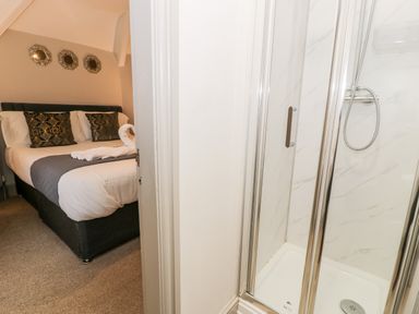 A bedroom with a double bed and decorative pillows next to a bathroom with a shower at Rose Suite in Barmouth