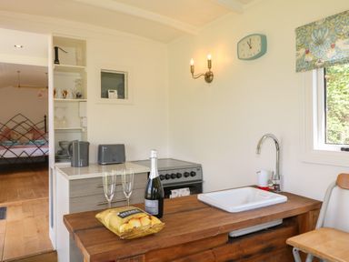 A kitchen area with a wooden countertop sink a bottle of prosecco two glasses and a bag of crisps at Shepherds Hut Colton near Rugeley Staffordshire