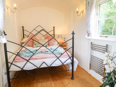A bedroom with a black metal bed frame a wooden floor and a window with floral curtains at Shepherds Hut in Colton near Rugeley Staffordshire