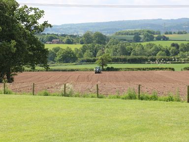 A tractor working on a plowed field with green grass and trees in the background at Shepherds Hut in Colton near Rugeley Staffordshire