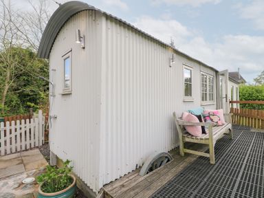 An exterior view of a corrugated metal shepherds hut with a wooden bench and cushions on the deck at Shepherds Hut in Colton near Rugeley Staffordshire