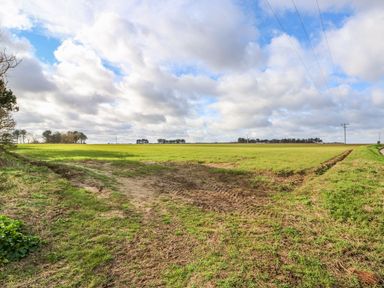 A rural field with tire tracks and power lines under a cloudy sky at The Nook in Mundesley