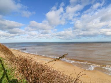 A sandy beach with wooden groynes extending into the sea under a partly cloudy sky at The Nook in Mundesley