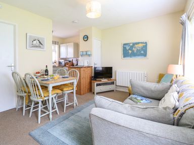 A living room with a grey sofa a dining table with chairs and a small kitchen area at The Nook in Mundesley