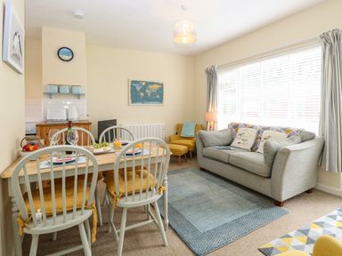 A dining table with four chairs and a sofa with cushions in a living room at The Nook Mundesley