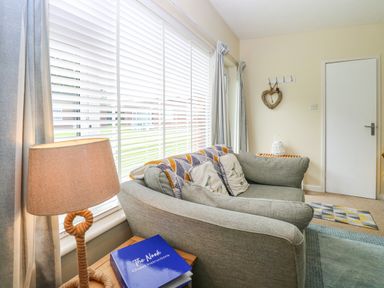 A living room with a sofa pillows lamp side table and window blinds at The Nook in Mundesley
