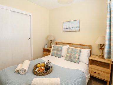 A bedroom with a bed with blue and plaid pillows and blanket two bedside tables with lamps and a tray with croissants and drinks on the bed at The Nook in Mundesley