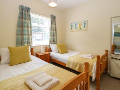 A bedroom with two single wooden beds yellow cushions and blankets a nightstand and a window with plaid curtains at The Nook in Mundesley