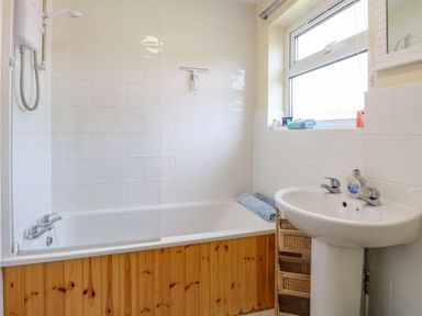 A bathroom with a bathtub shower sink and a window at The Nook in Mundesley