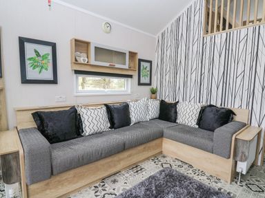 A living room with a gray sectional sofa with black and white cushions a patterned floor and wallpaper at Hares Rest Nantmel near Rhayader