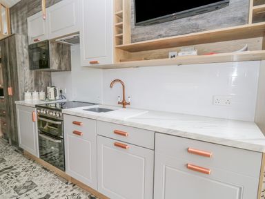 A kitchen with white cabinets copper handles a sink stove kettle microwave and patterned floor tiles at Hares Rest in Nantmel near Rhayader