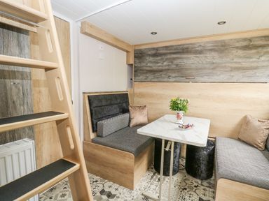 A small dining area with a white table surrounded by two bench seats with cushions a ladder and patterned floor at Hares Rest in Nantmel near Rhayader
