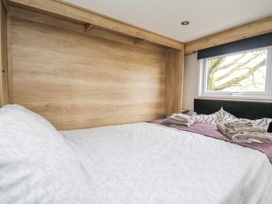 A bed with folded towels on a purple runner under a window with a view of tree branches at Hares Rest in Nantmel near Rhayader