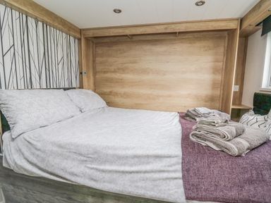 A bedroom with a bed made with white sheets and pillows and folded towels on a purple blanket at Hares Rest in Nantmel near Rhayader