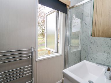 A bathroom with a white sink a chrome towel radiator an open window and a glass shower enclosure at Hares Rest Nantmel near Rhayader