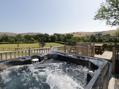 A hot tub on a wooden deck with a view of fields and hills at Hares Rest in Nantmel near Rhayader