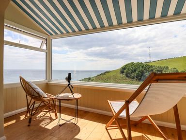 A sunroom with two chairs a small round table and a telescope overlooking the sea and hillside at Ocean View in Downderry