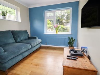 A living room with a blue sofa wooden floor a wooden table with gaming consoles and a wall-mounted TV at Ocean View in Downderry