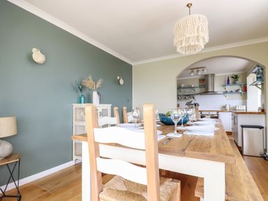 A dining area with a wooden table set with plates and glasses next to a kitchen visible through an archway at Ocean View in Downderry
