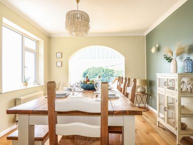 A dining room with a wooden table set with plates and glasses and wooden chairs at Ocean View in Downderry