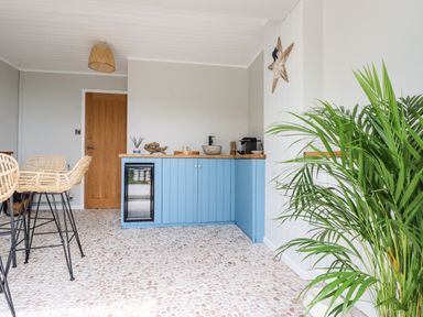 A kitchen area with blue cabinets a small fridge and a wooden dining table with wicker chairs at Ocean View Downderry
