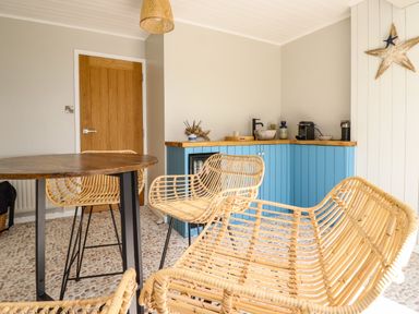 A dining area with wicker chairs around a wooden table and a blue cabinet with a coffee machine at Ocean View in Downderry