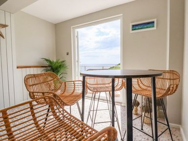 A dining area with wicker chairs and a round table near a window with a view of the sea at Ocean View in Downderry