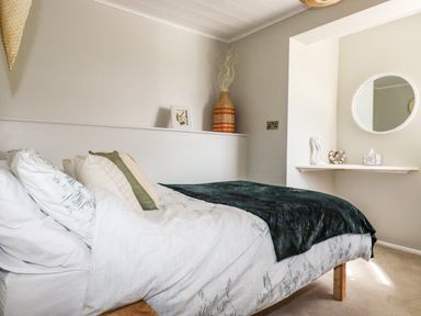 A bedroom with a bed with pillows and a blanket a shelf with decorative items and a round mirror at Ocean View Downderry