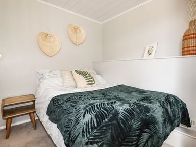 A bedroom with a bed covered in green leaf patterned blanket and two straw decorations on the wall at Ocean View in Downderry