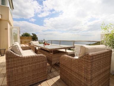 A balcony with wicker furniture and a glass table overlooking the sea at Ocean View in Downderry