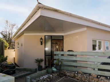 The entrance of a single-story house with a wooden door and three small windows by a light hanging on the wall at Ocean View in Downderry