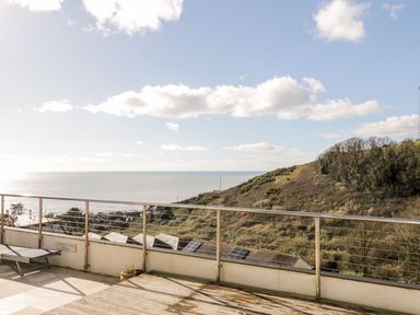 A balcony with railing and a lounge chair overlooking a hill and the sea at Ocean View in Downderry