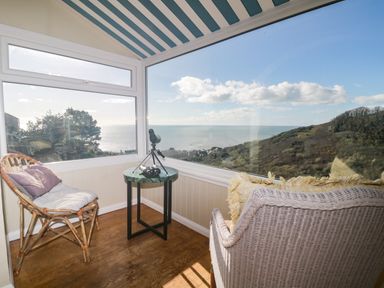 A sunroom with wicker chairs a small round table with binoculars and a telescope overlooking the sea and hills at Ocean View in Downderry