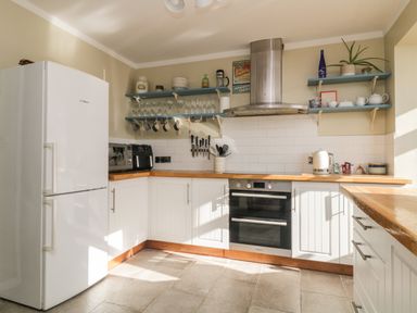 A kitchen with white cabinets wooden countertops a white refrigerator and blue shelves holding dishes at Ocean View in Downderry